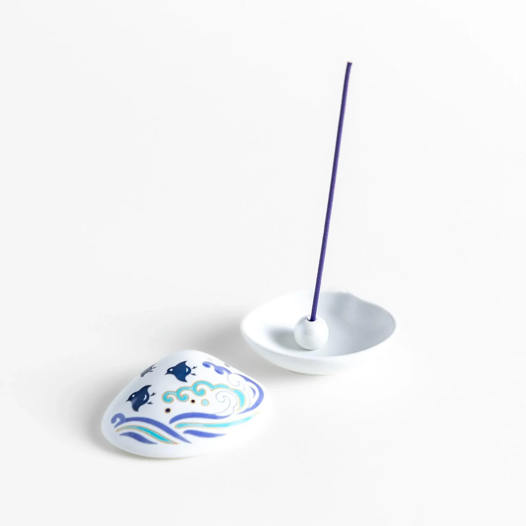 White seashell-shaped ceramic incense holder with blue wave and seabird motif and rounded holder for secure placement.