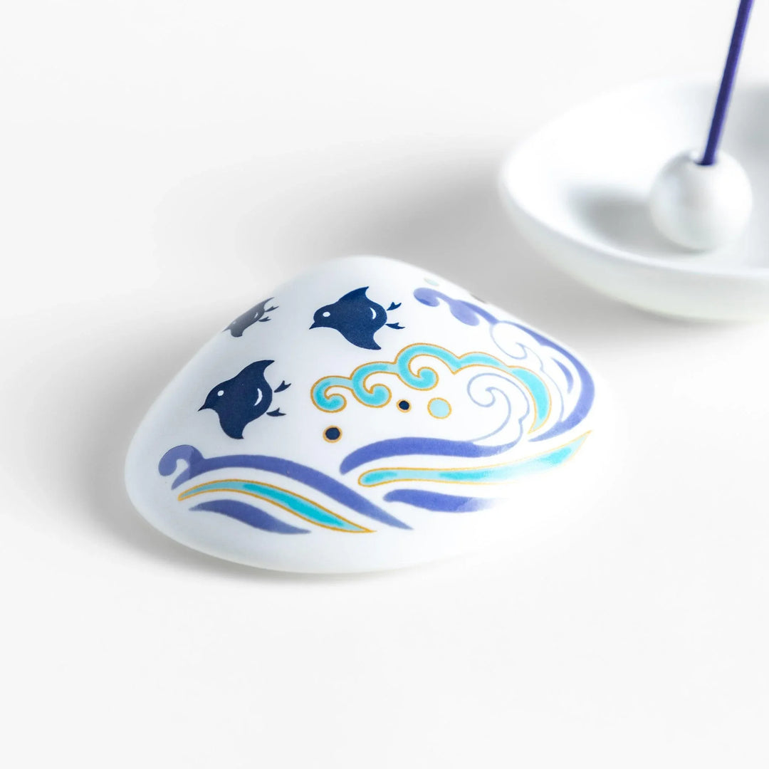 White seashell-shaped ceramic incense holder with blue wave and seabird motif and rounded holder for secure placement.
