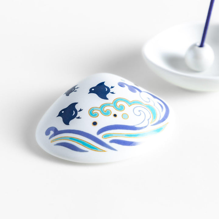 White seashell-shaped ceramic incense holder with blue wave and seabird motif and rounded holder for secure placement.