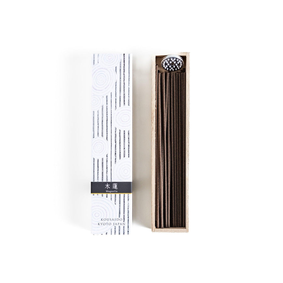 Japanese magnolia incense in wooden box with brown sticks and white design accented with black patterns.