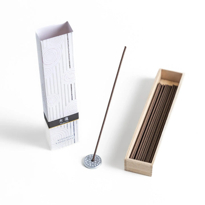 Japanese magnolia incense in wooden box with brown sticks and white design accented with black patterns.