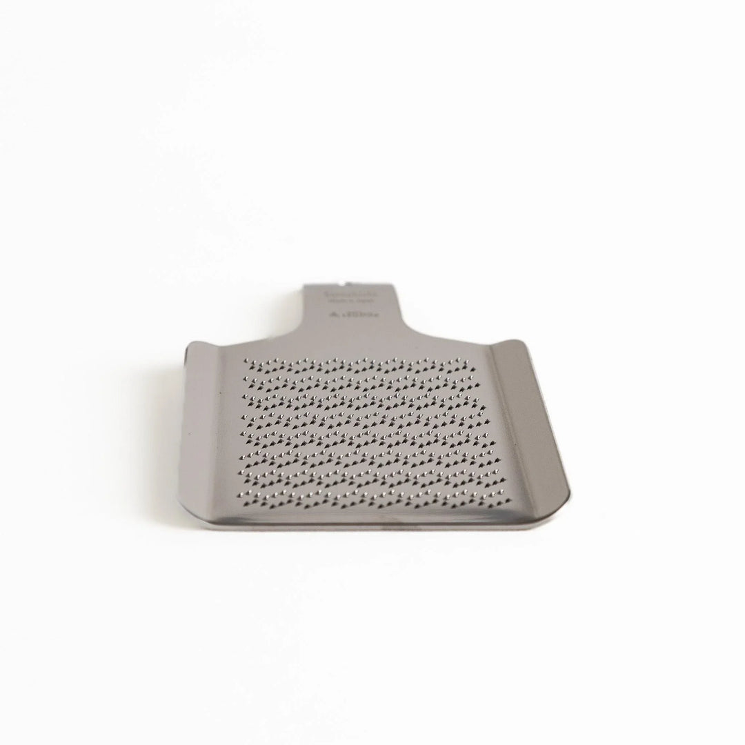 Stainless steel wasabi grater with wave pattern ideal for finely grating fresh wasabi root in Japanese cooking.