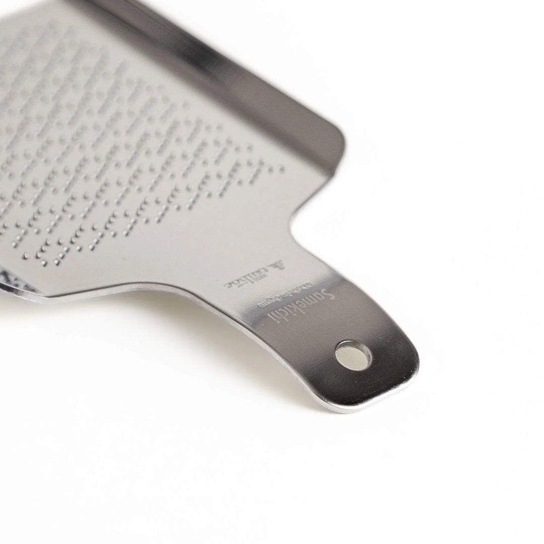 Stainless steel wasabi grater with wave pattern ideal for finely grating fresh wasabi root in Japanese cooking.
