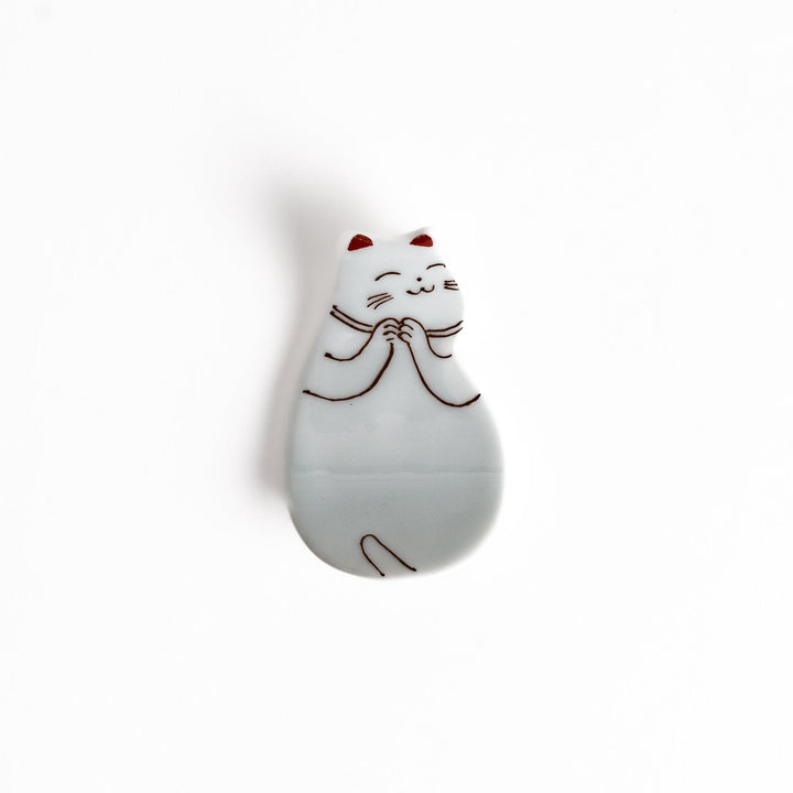 Ceramic chopstick rest shaped like sleeping cat with brown and red lines and glossy white glaze finish.