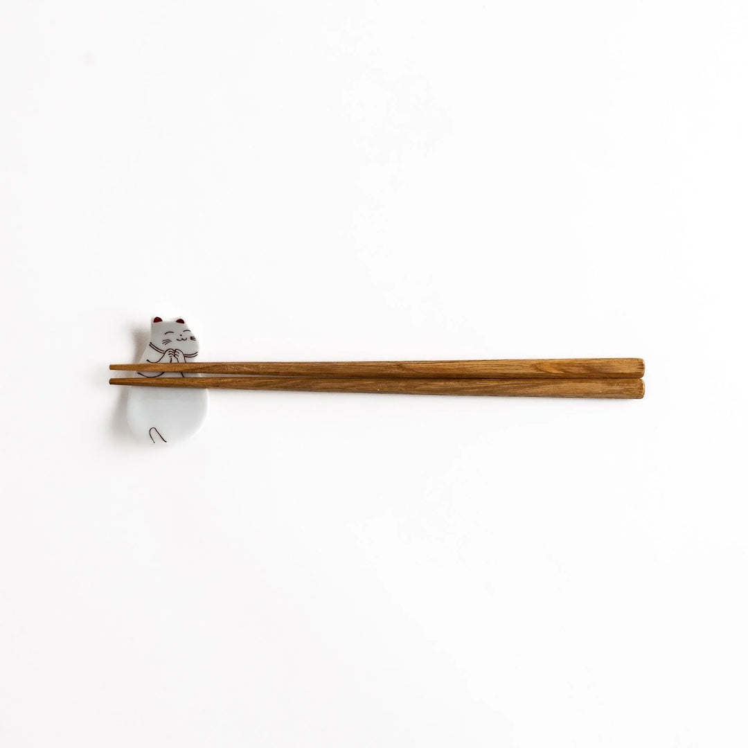 Ceramic sleeping cat-shaped chopsticks rest with chopsticks placed, showcasing its elegant brown and red line art details.