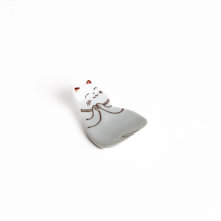 Ceramic chopstick rest shaped like sleeping cat with brown and red lines and glossy white glaze finish.