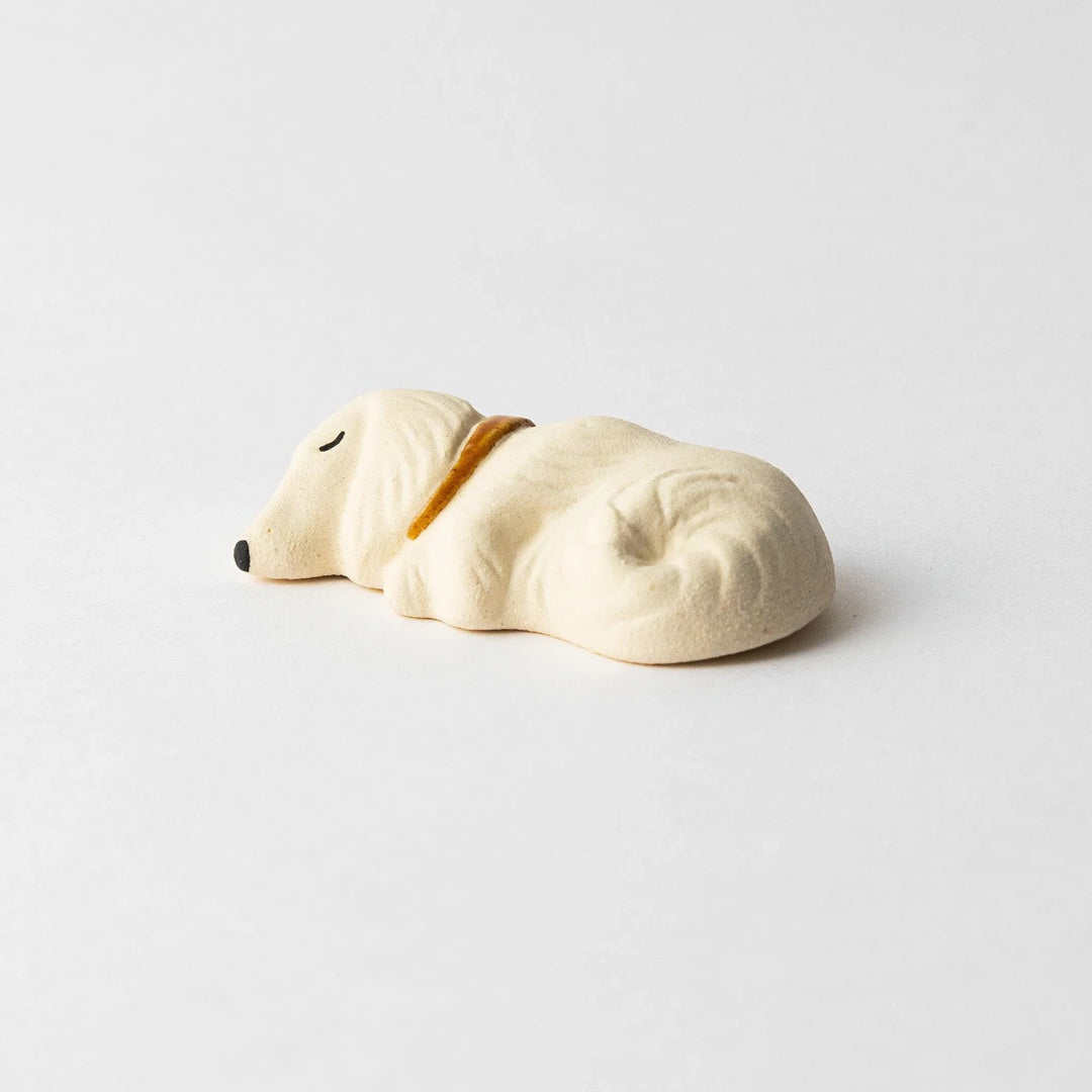 Side view of a white ceramic chopstick rest shaped like a sleeping dog, showing its detailed contours and gold collar.