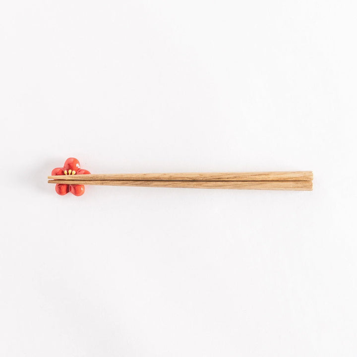 Red plum chopsticks rest with wooden chopsticks placed on it.