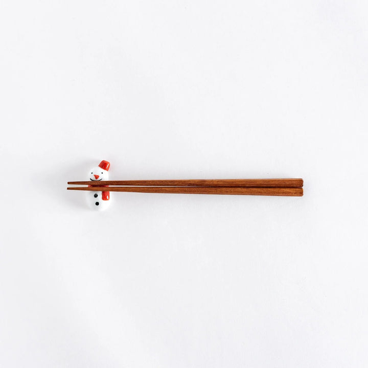 A wide view of the red-scarfed snowman chopstick rest with chopsticks placed on it, showcasing its playful design.