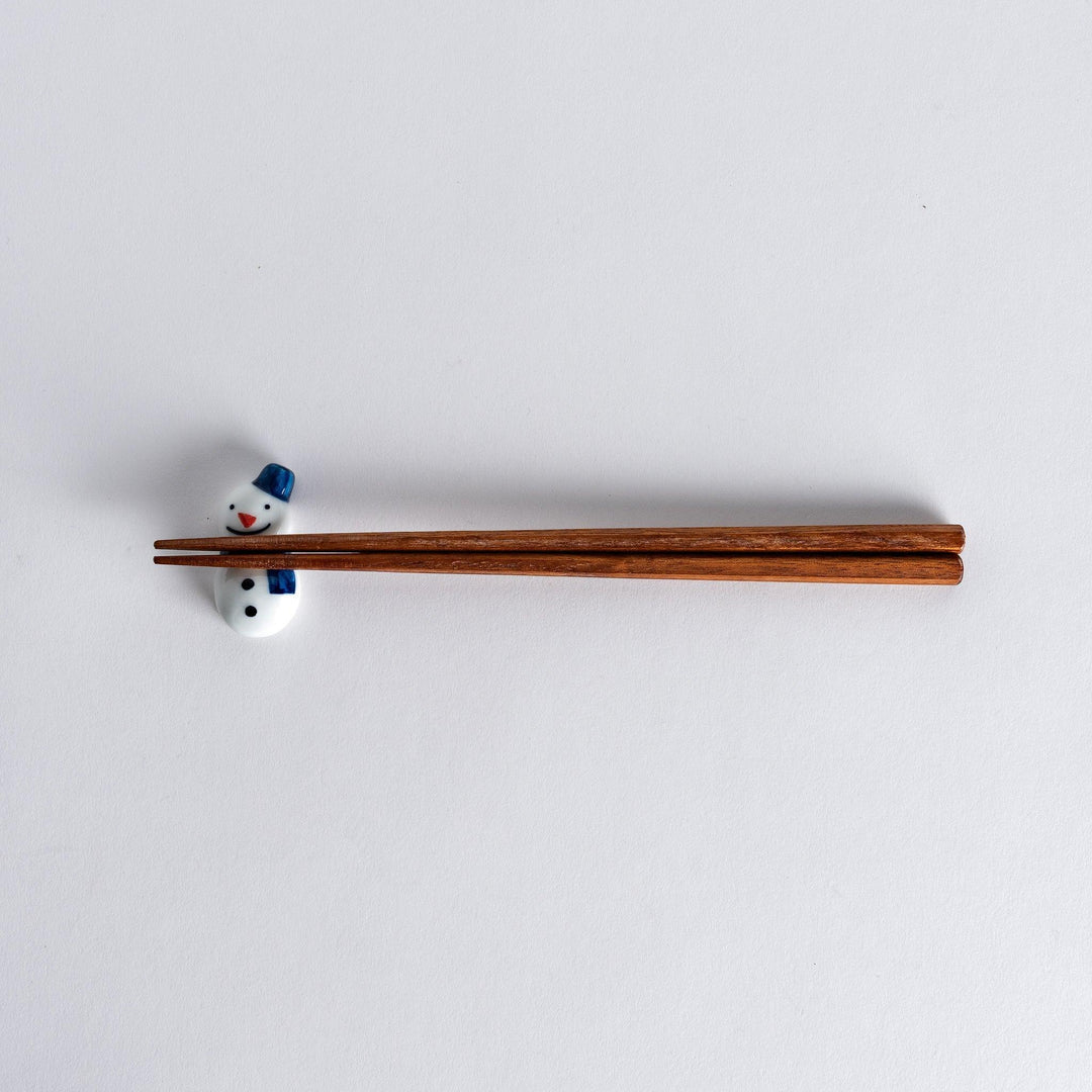 Snowman shaped ceramic chopstick rest with scarf detail adding cheerful winter charm to Japanese table setting.