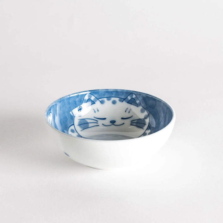 A dessert bowl with a chubby blue-spotted cat, looking peaceful and content.