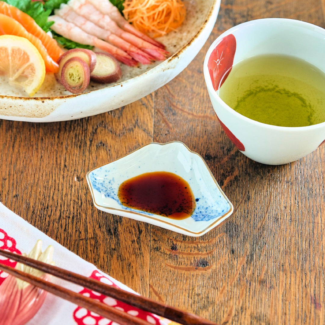 Mount Fuji shaped mini Japanese sauce dish with blue ink pattern filled with soy sauce beside sashimi set.