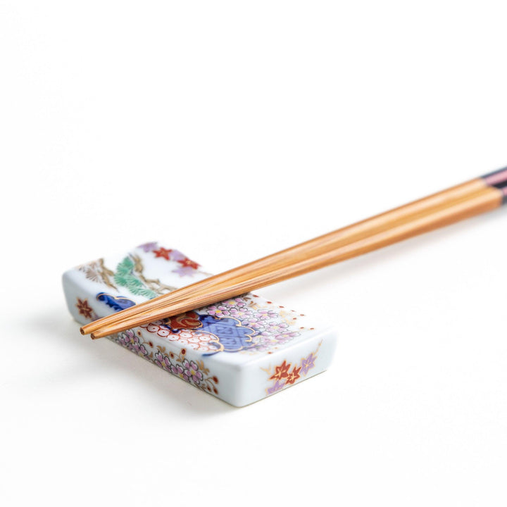 Rectangular ceramic chopstick rest with blue red and green Japanese patterns for decorative table setting.