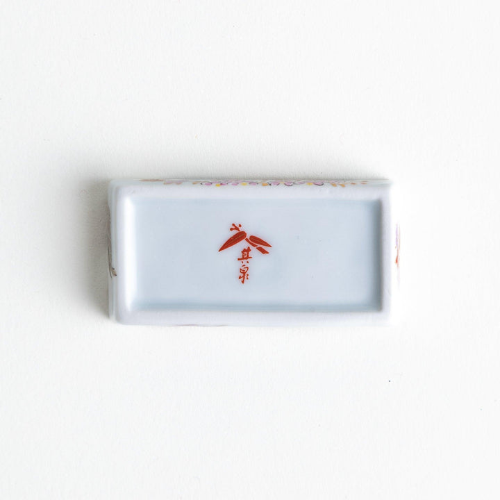 Rectangular ceramic chopstick rest with blue red and green Japanese patterns for decorative table setting.