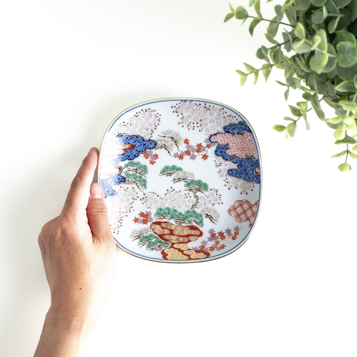 Square dessert plate with Japanese landscape design of trees and clouds bordered by red and blue patterns.