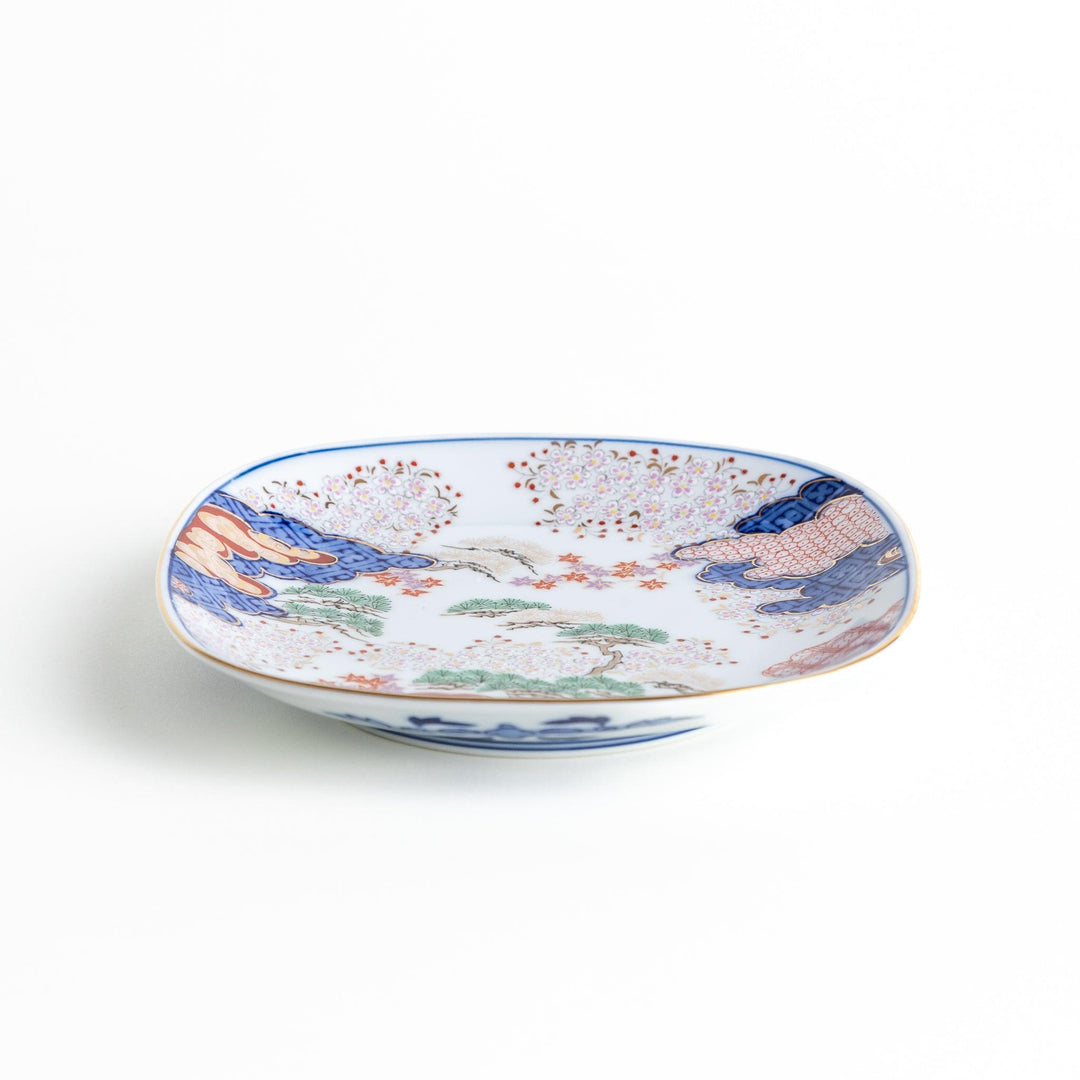 Square dessert plate with Japanese landscape design of trees and clouds bordered by red and blue patterns.