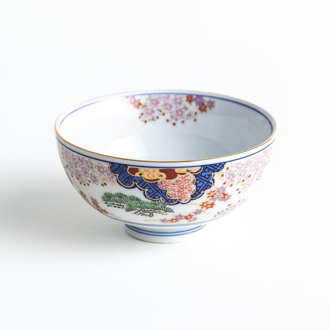 Round ceramic rice bowl with traditional Japanese tree and cloud designs in blue red and green on white.