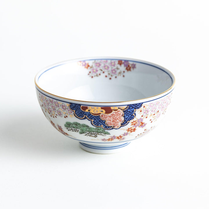 Round ceramic rice bowl with traditional Japanese tree and cloud designs in blue red and green on white.