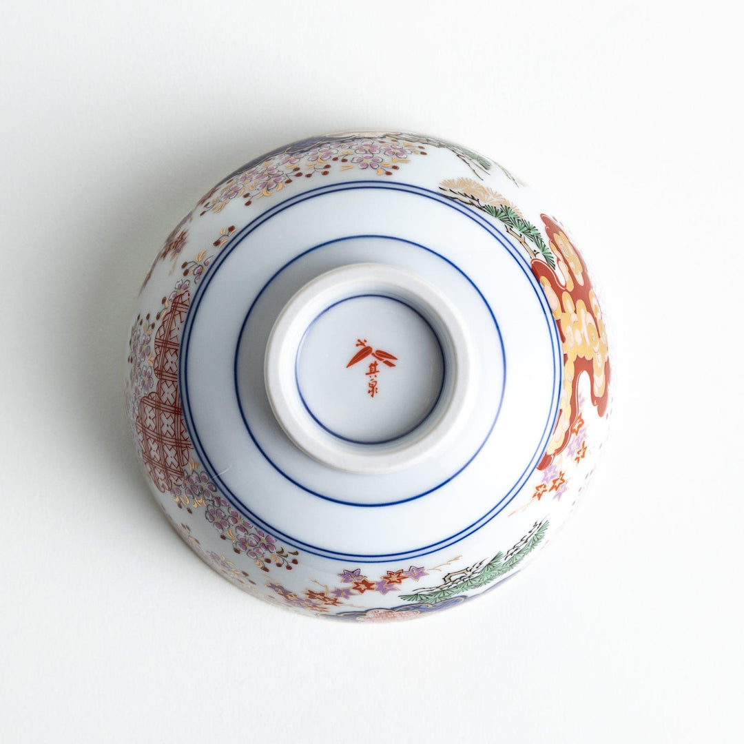 Round ceramic rice bowl with traditional Japanese tree and cloud designs in blue red and green on white.