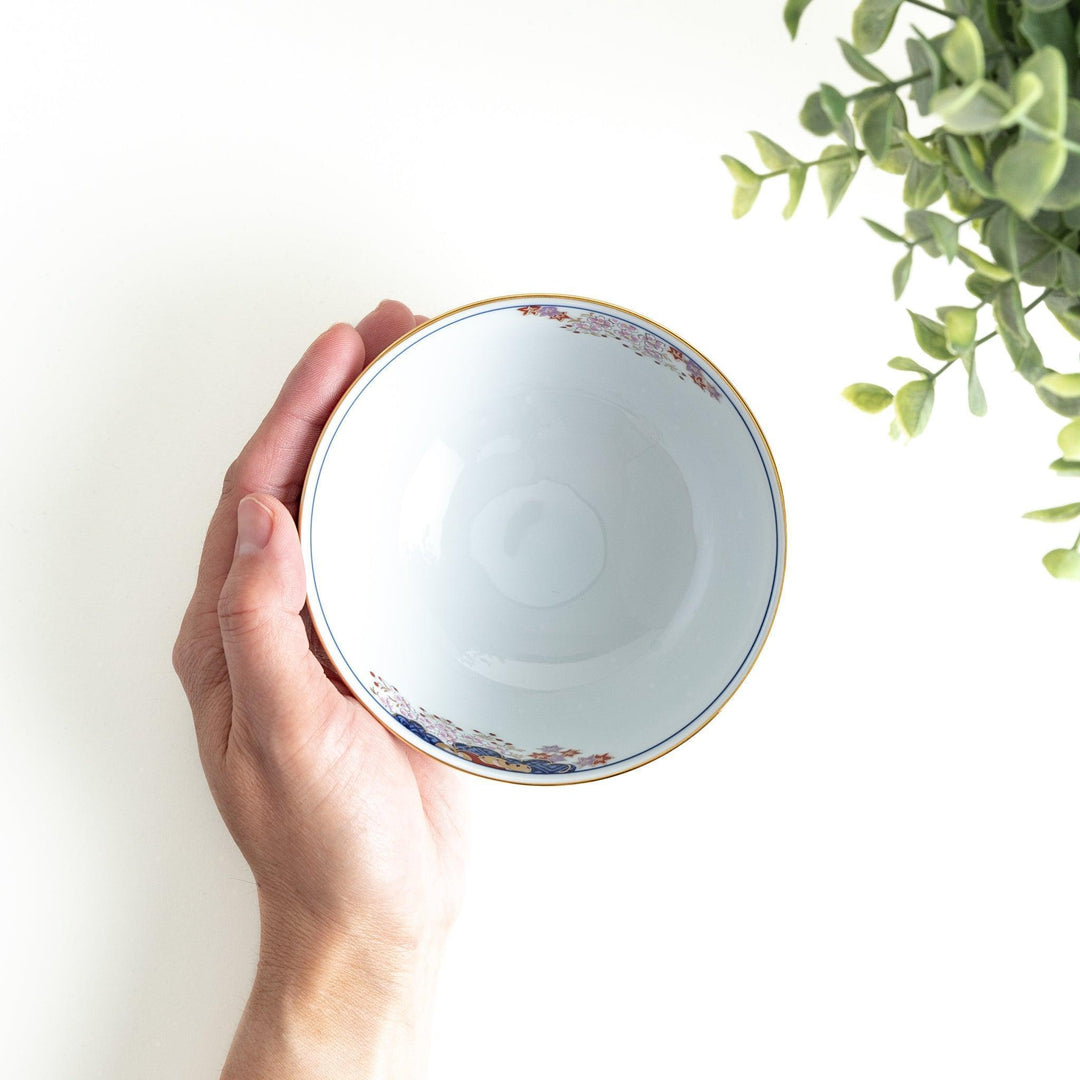 Round ceramic rice bowl with traditional Japanese tree and cloud designs in blue red and green on white.