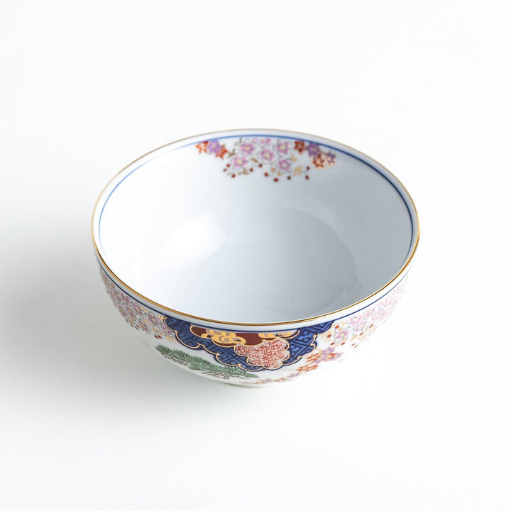 Round ceramic rice bowl with traditional Japanese tree and cloud designs in blue red and green on white.