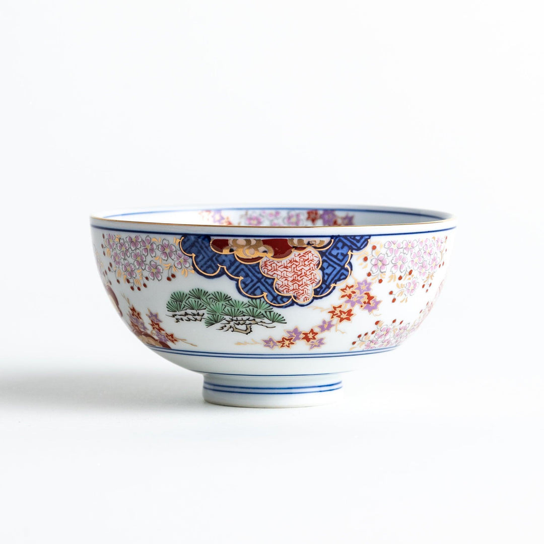 Round ceramic rice bowl with traditional Japanese tree and cloud designs in blue red and green on white.