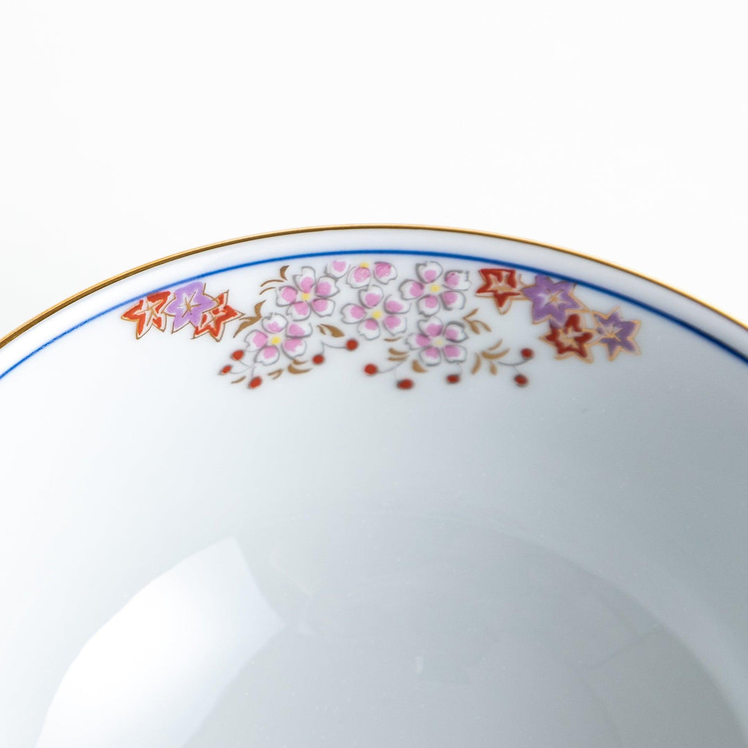 Round ceramic rice bowl with traditional Japanese tree and cloud designs in blue red and green on white.