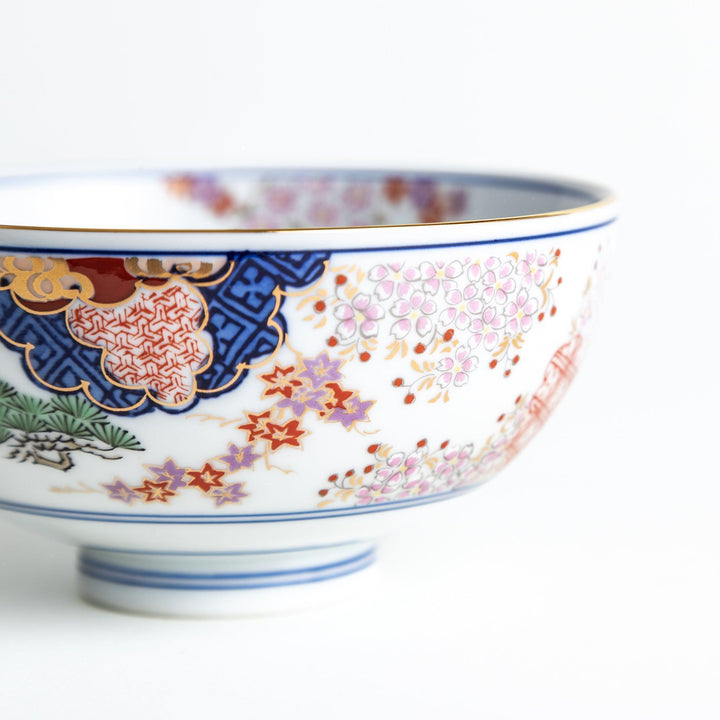 Round ceramic rice bowl with traditional Japanese tree and cloud designs in blue red and green on white.