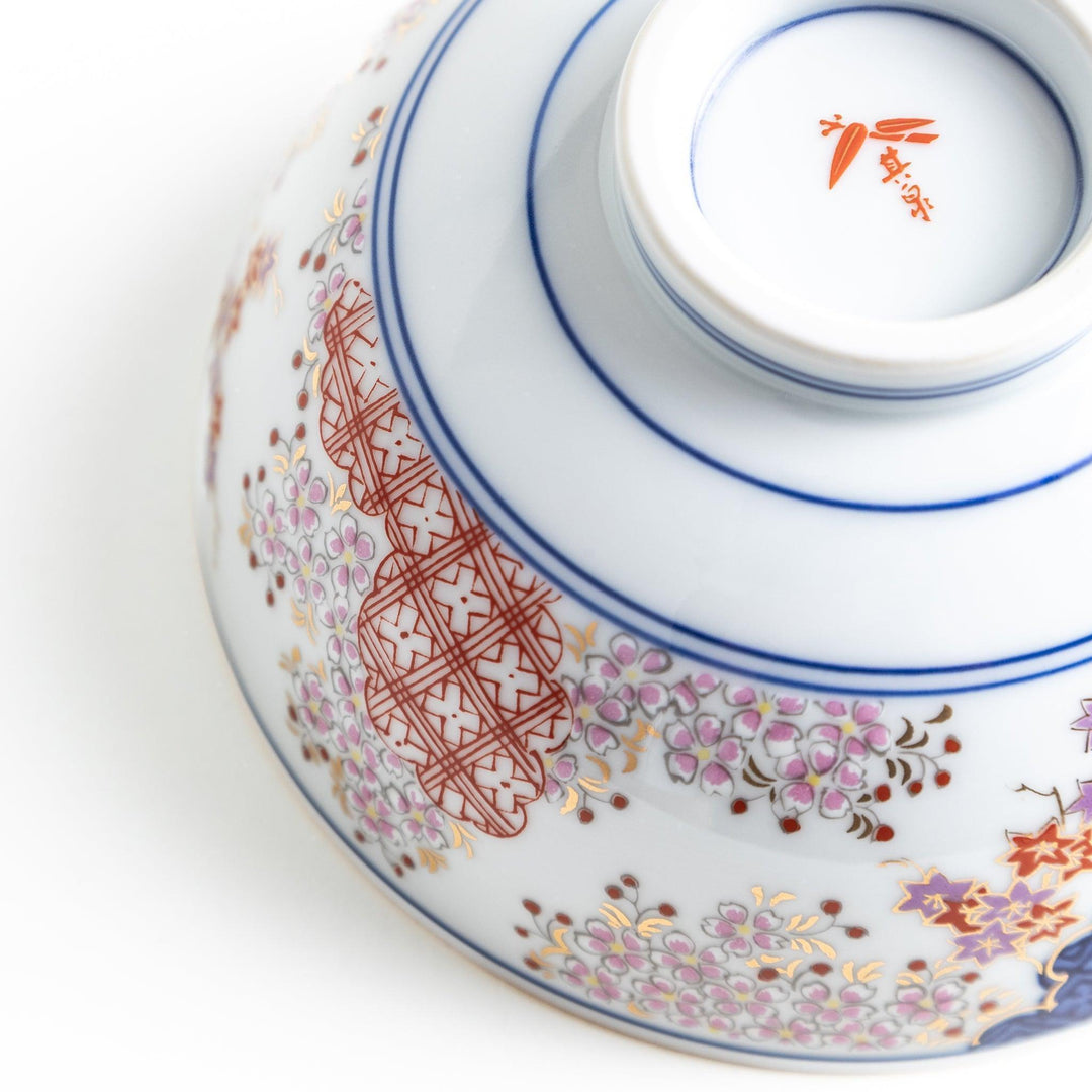Round ceramic rice bowl with traditional Japanese tree and cloud designs in blue red and green on white.