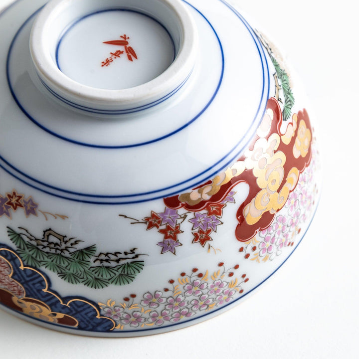 Round ceramic rice bowl with traditional Japanese tree and cloud designs in blue red and green on white.