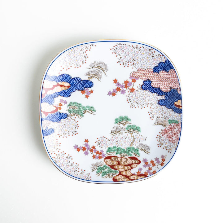 Square salad plate with Japanese landscape of trees clouds and maple leaves framed by blue red patterns.