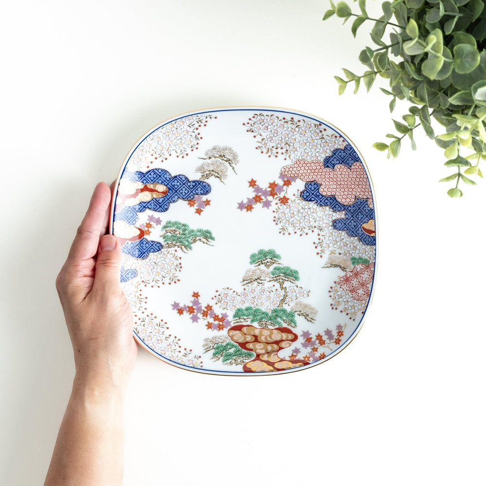 Square salad plate with Japanese landscape of trees clouds and maple leaves framed by blue red patterns.