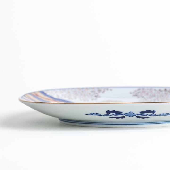 Square salad plate with Japanese landscape of trees clouds and maple leaves framed by blue red patterns.