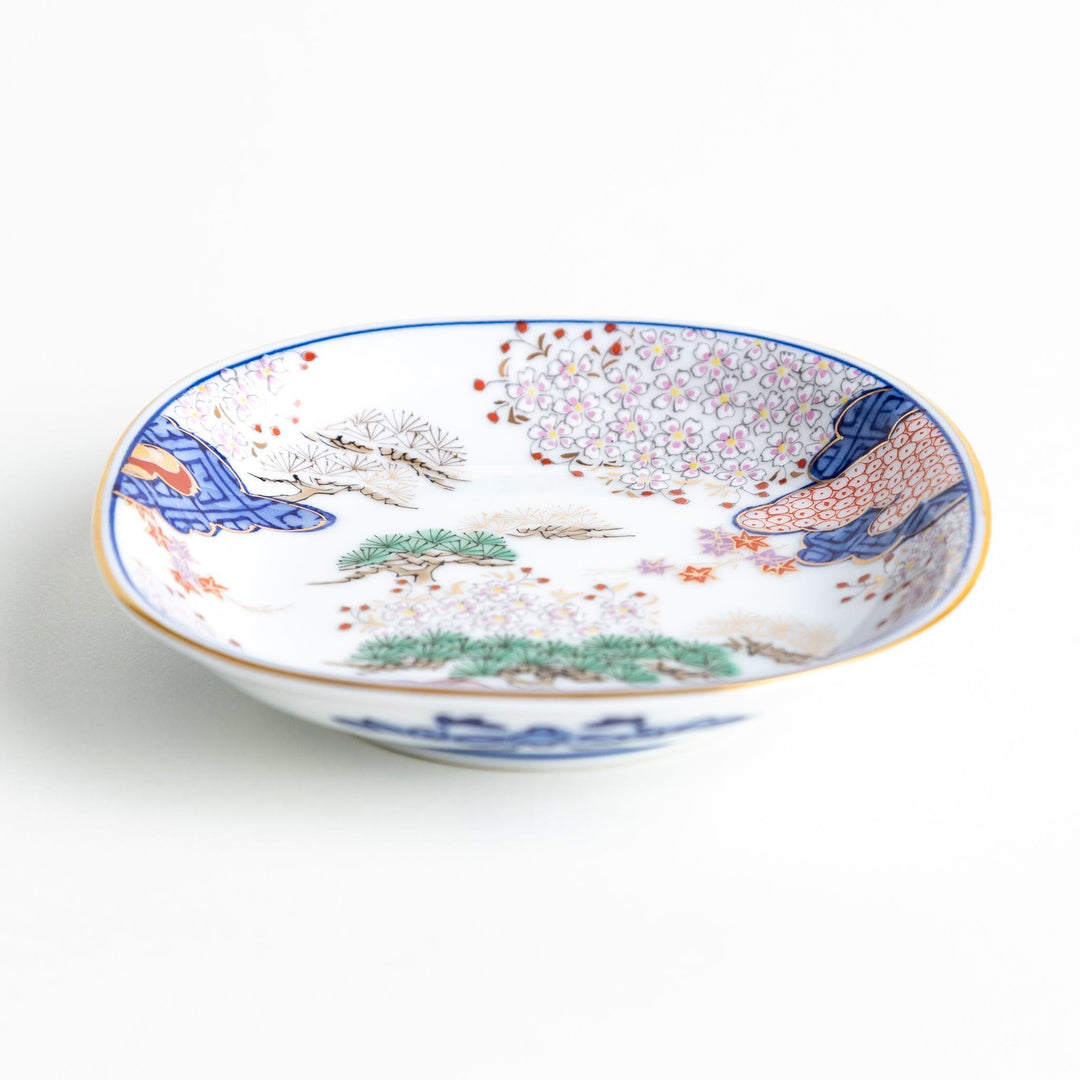 Square Japanese sauce dish with landscape trees clouds and golden sun bordered by blue and red patterns.