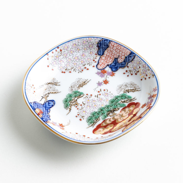 Square Japanese sauce dish with landscape trees clouds and golden sun bordered by blue and red patterns.