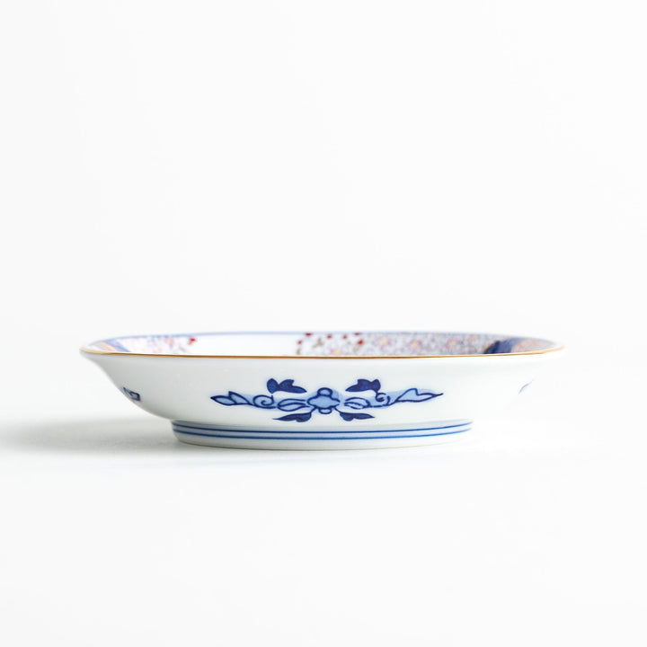 Square Japanese sauce dish with landscape trees clouds and golden sun bordered by blue and red patterns.