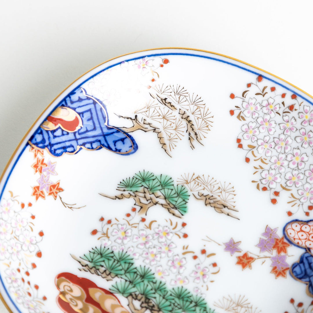 Square Japanese sauce dish with landscape trees clouds and golden sun bordered by blue and red patterns.