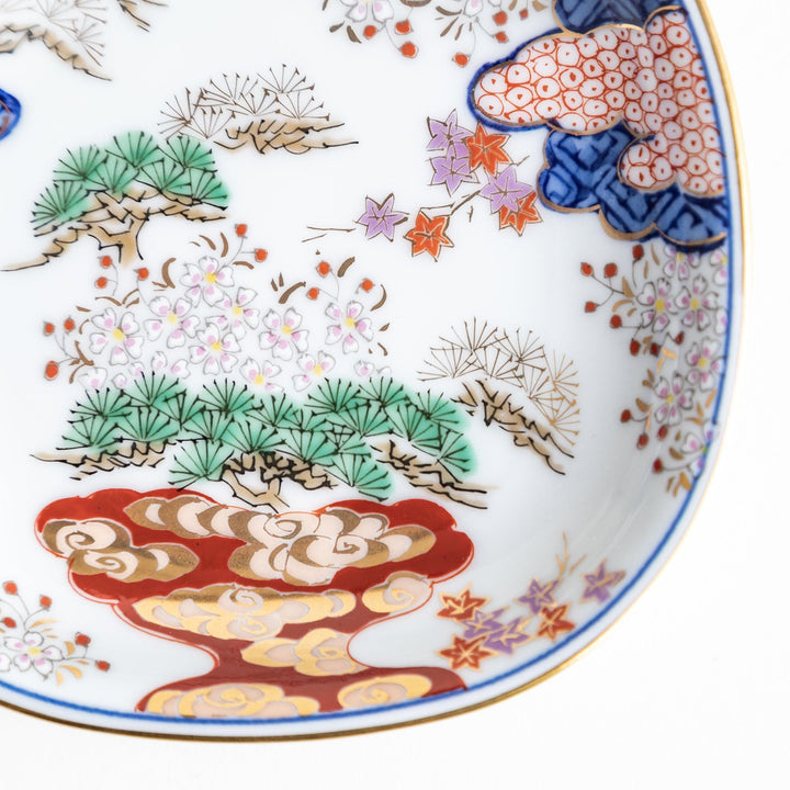 Square Japanese sauce dish with landscape trees clouds and golden sun bordered by blue and red patterns.