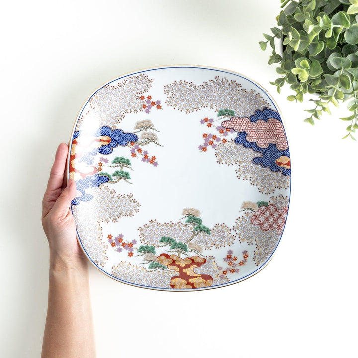 Square serving plate with white base featuring Japanese landscape of trees clouds and red maple leaves.