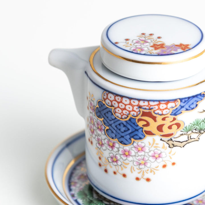 White Japanese sauce dispenser with blue red and gold patterns and matching saucer for elegant serving.