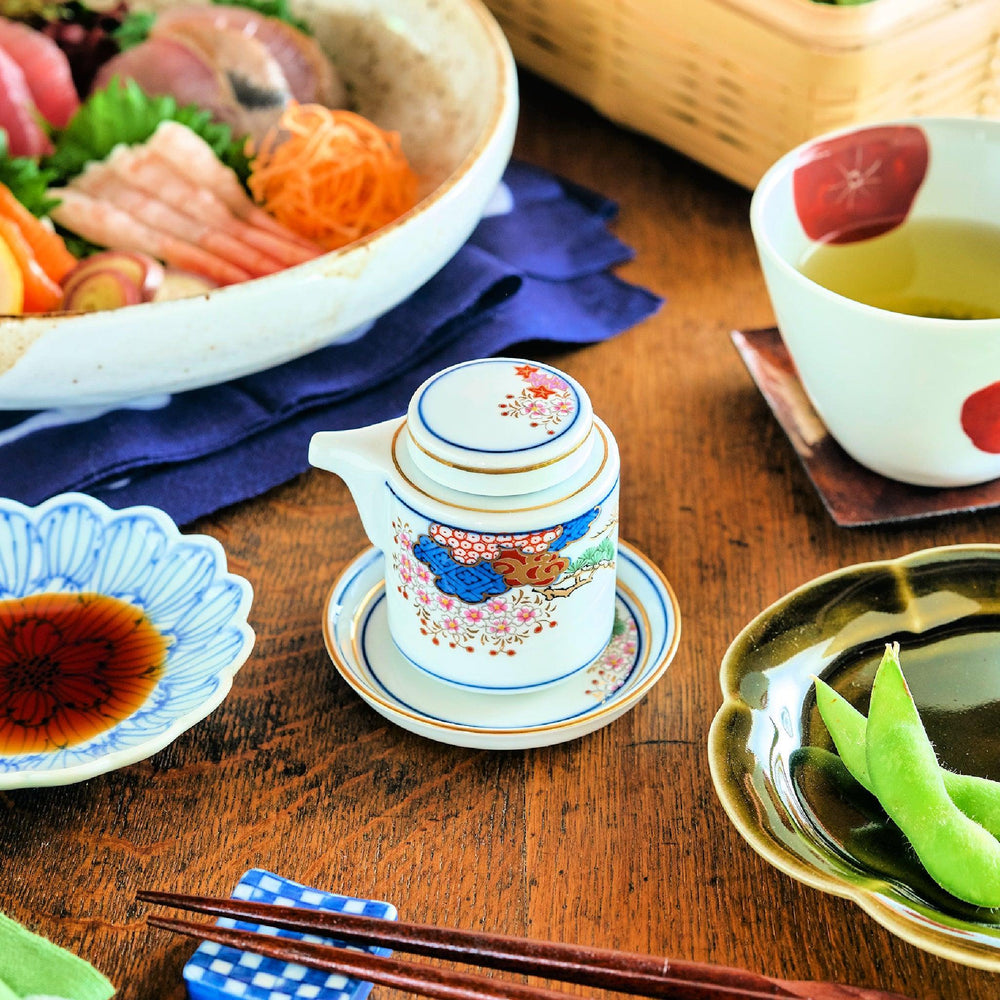 White Japanese sauce dispenser with blue red and gold patterns and matching saucer for elegant serving.