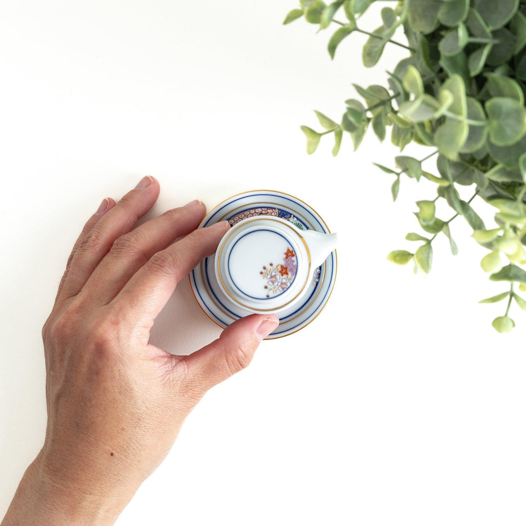 White Japanese sauce dispenser with blue red and gold patterns and matching saucer for elegant serving.
