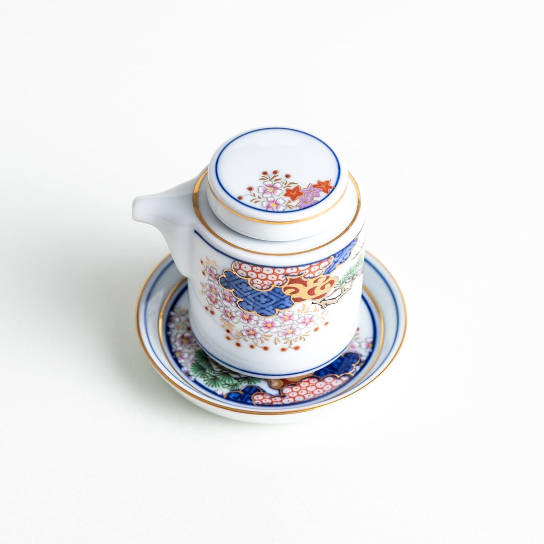 White Japanese sauce dispenser with blue red and gold patterns and matching saucer for elegant serving.