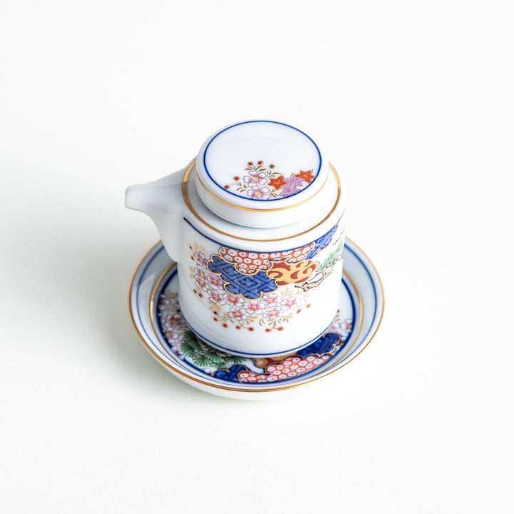 White Japanese sauce dispenser with blue red and gold patterns and matching saucer for elegant serving.