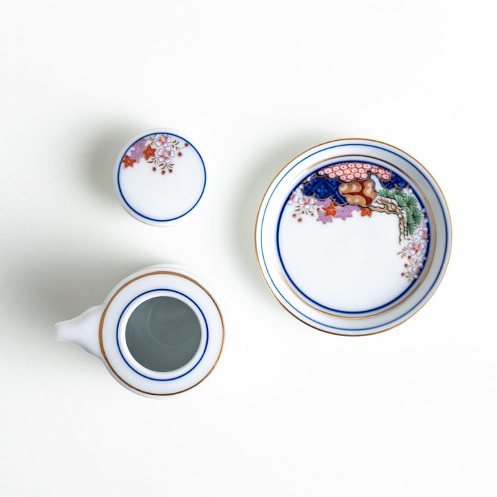 White Japanese sauce dispenser with blue red and gold patterns and matching saucer for elegant serving.