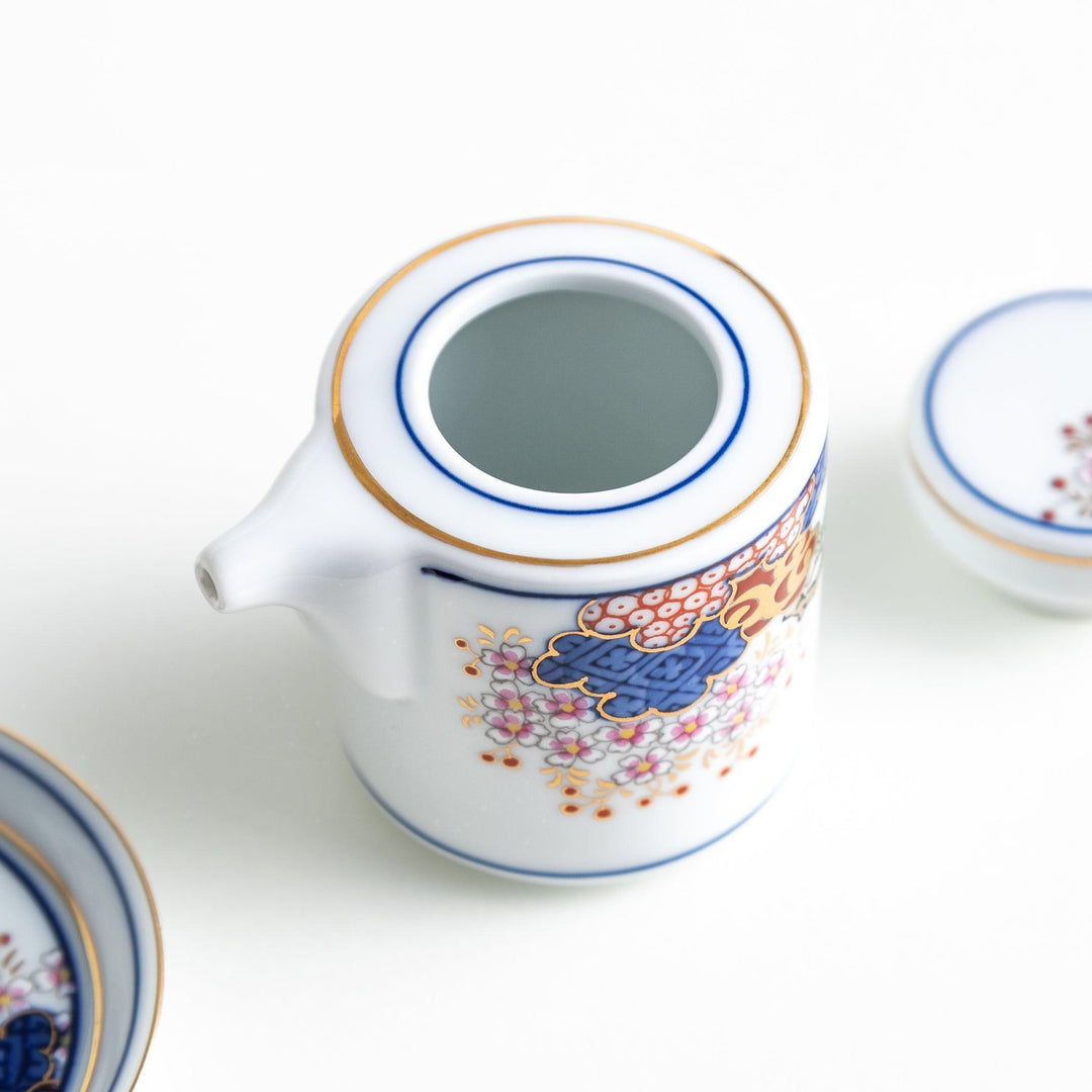 White Japanese sauce dispenser with blue red and gold patterns and matching saucer for elegant serving.