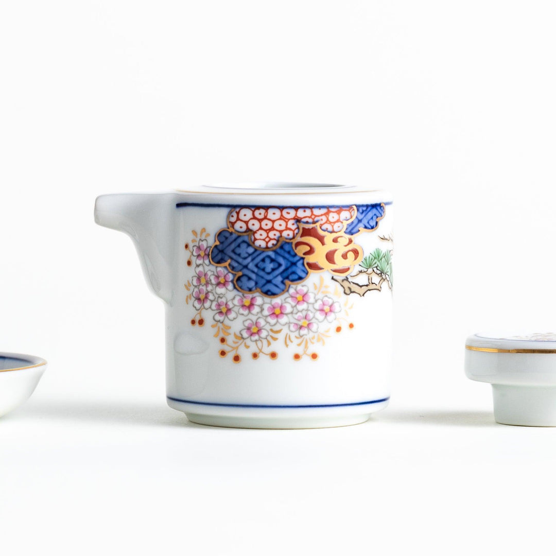 White Japanese sauce dispenser with blue red and gold patterns and matching saucer for elegant serving.
