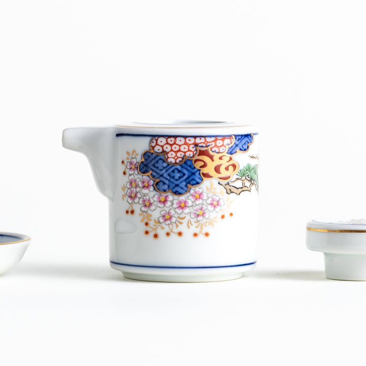 White Japanese sauce dispenser with blue red and gold patterns and matching saucer for elegant serving.