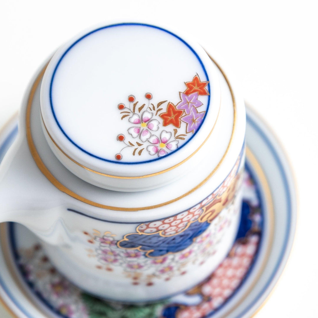 White Japanese sauce dispenser with blue red and gold patterns and matching saucer for elegant serving.