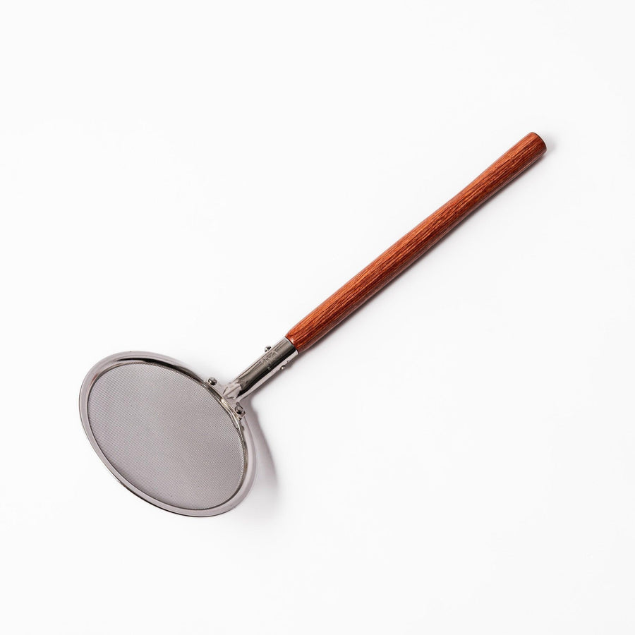 Stainless steel round-mesh skimmer with long wooden handle, perfect for straining soups and frying in home kitchens.